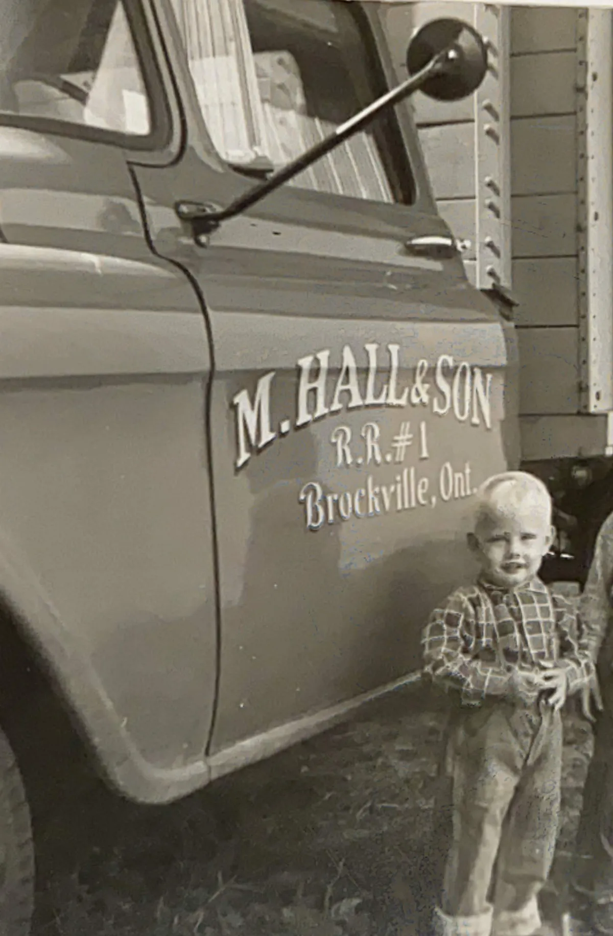 Two small boys in plaid shirts beside a farm truck lettered “M. Hall & Son, R.R. #1, Brockville, Ont.” and “Apples for health”