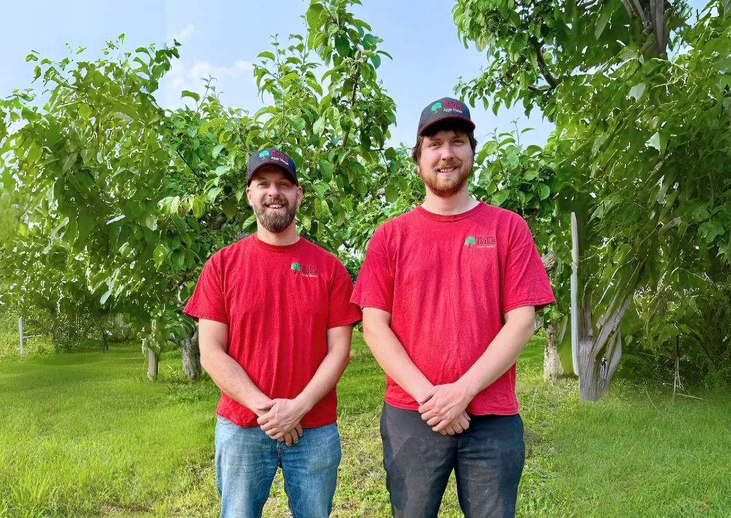 Matthew Shapton and Kyle Hall in red Hall’s shirts and caps, standing in the orchard